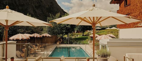 A poolside area with lounge chairs and umbrellas, a clear sky, and a mountain in the background.