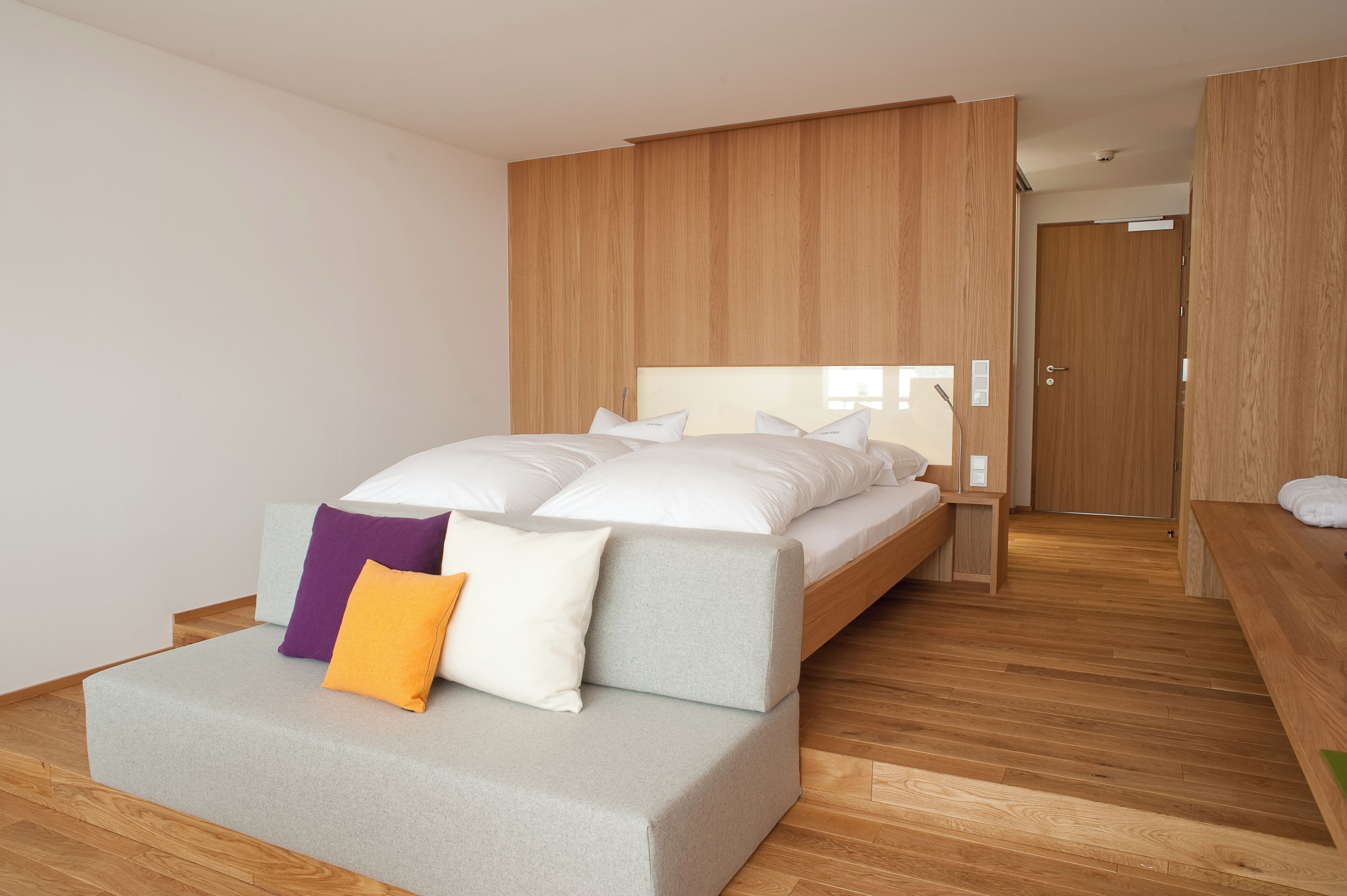 A modern bedroom with a bed, a bench, and a wooden wardrobe.
