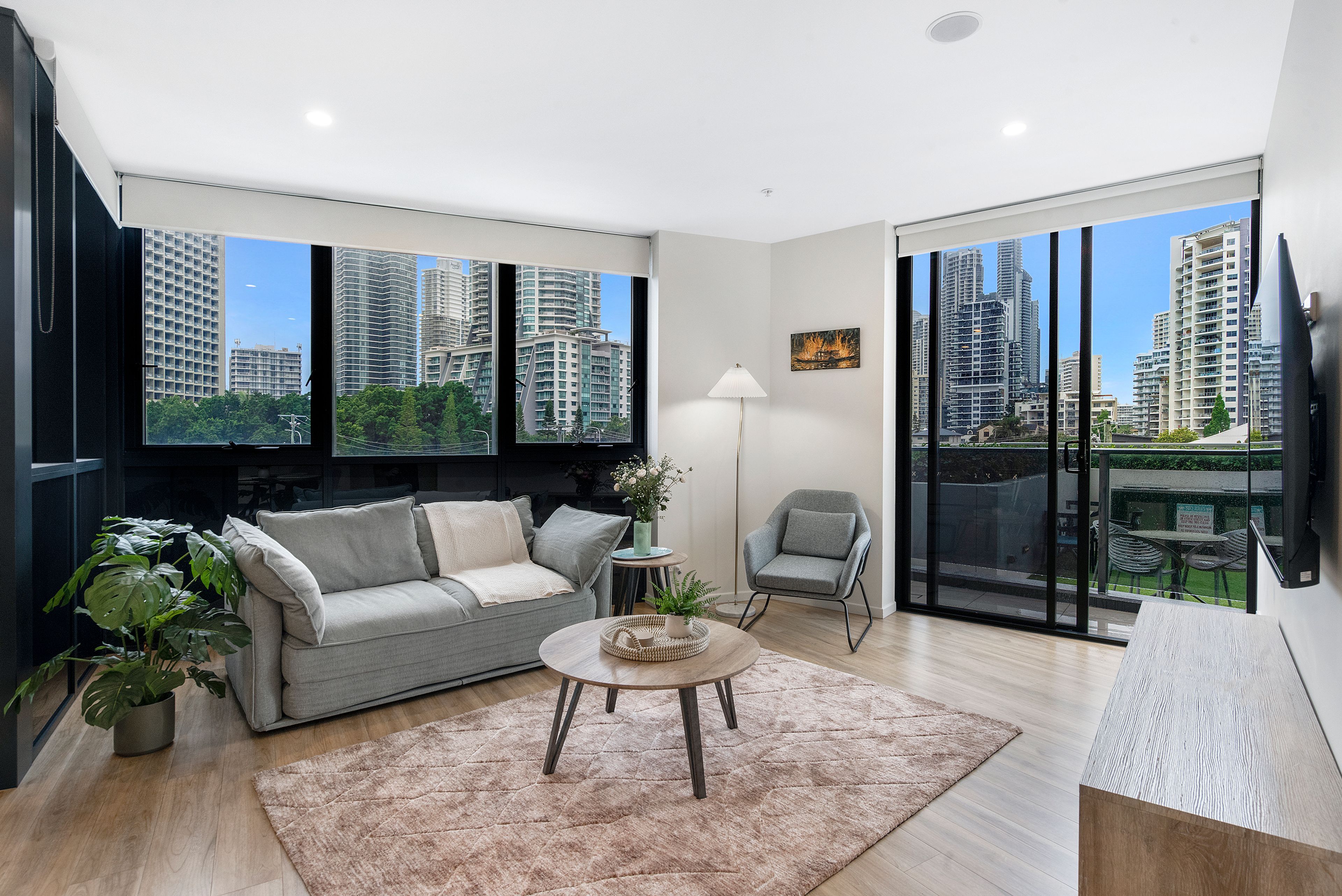 Una sala de estar moderna con un sofá, una mesa de centro y un sillón. Amplias ventanas con vista a la ciudad.