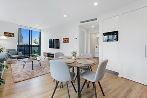 A modern living room with a dining area, large windows, and a flat-screen TV mounted on the wall.