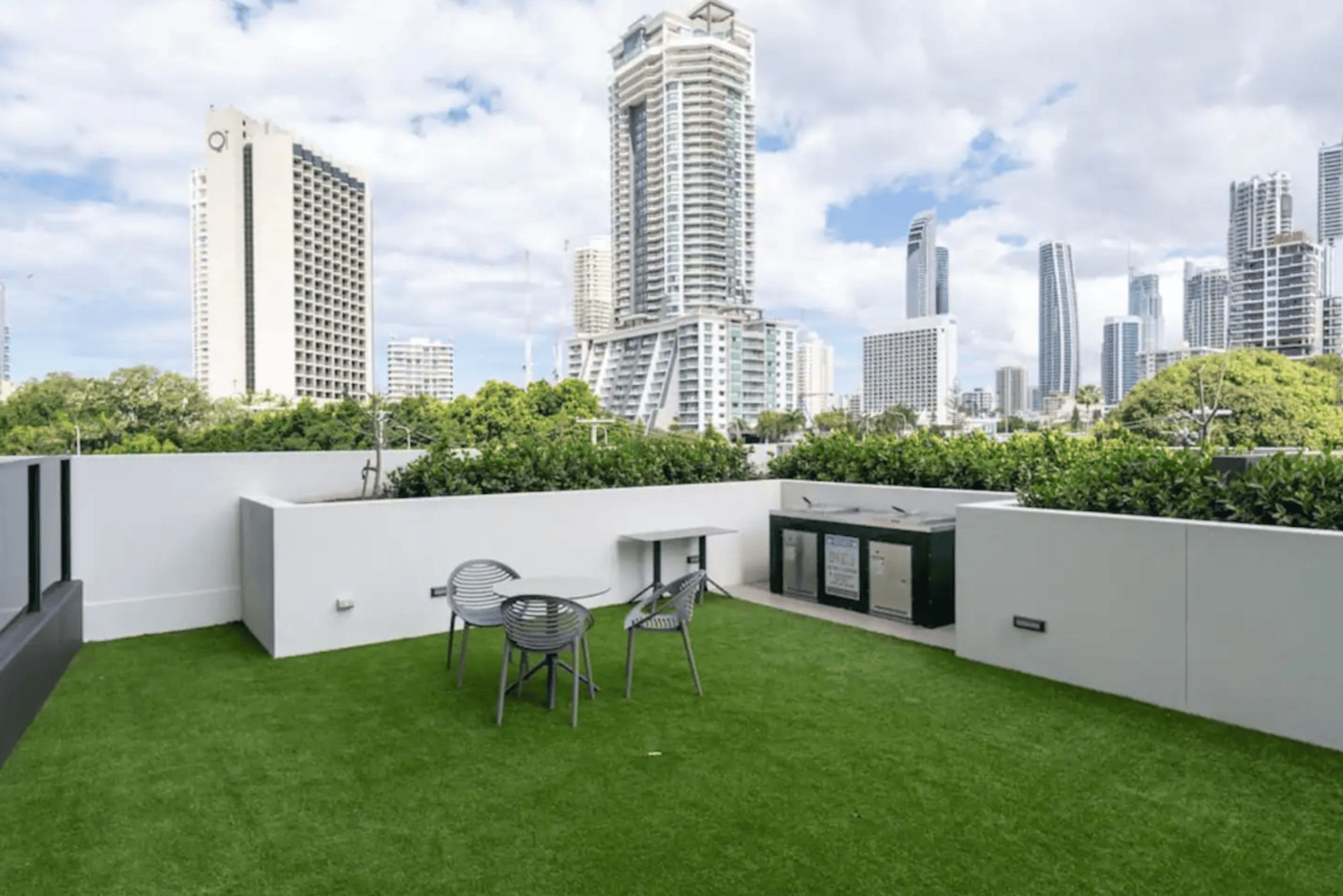 A rooftop terrace with artificial grass, a table, two chairs, and a small grill area.