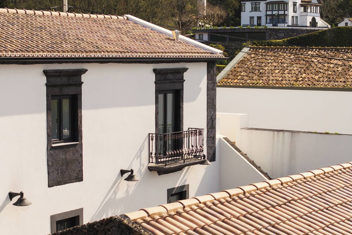 A building with a tiled roof, a balcony with a wrought iron railing, and a window with a stone base.