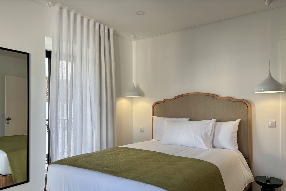 A neatly made bed with white and green bedding, a wooden headboard, and two pendant lights.