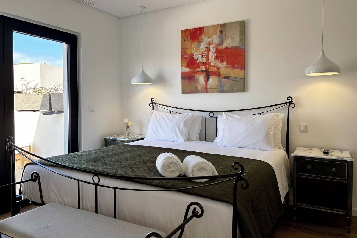 A modern bedroom with a bed, bedside tables, a bench, and a large window.
