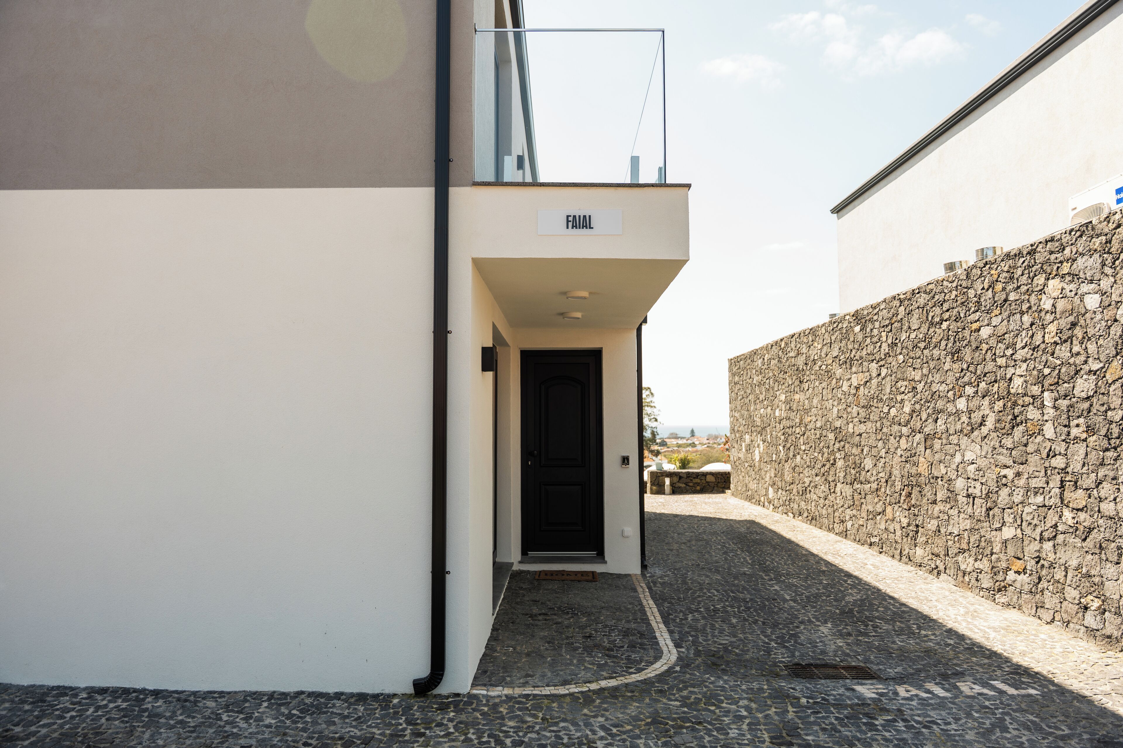 A narrow alleyway leading to a building with a stone wall and a sign reading "FAIAL".