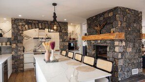 A modern kitchen with a large island, stone walls, and a built-in fireplace. - Azores Homes Resort & Spa (Ponta Delgada)