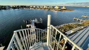 Una propiedad frente al agua con un muelle, una escalera que lleva a una terraza, y vistas de casas al otro lado del agua.