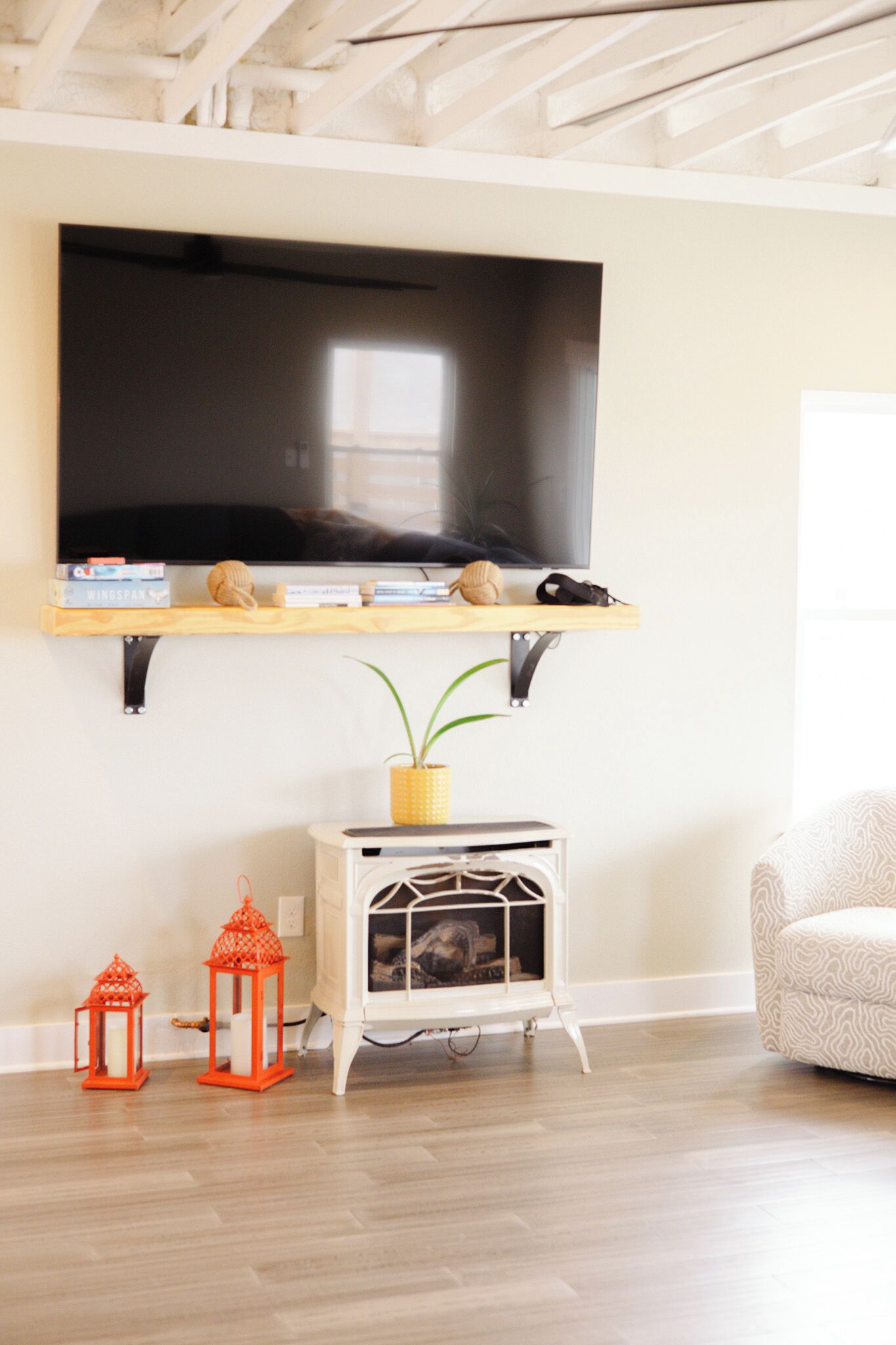 A living room with a mounted TV, a white cabinet, two red lanterns, and a patterned sofa.