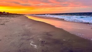 Una playa con un atardecer, olas y una costa lejana.