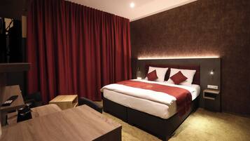 Ein modernes Hotelzimmer mit einem großen Bett, roten Vorhängen, einem Holztisch und einem Nachttisch mit Lampe.