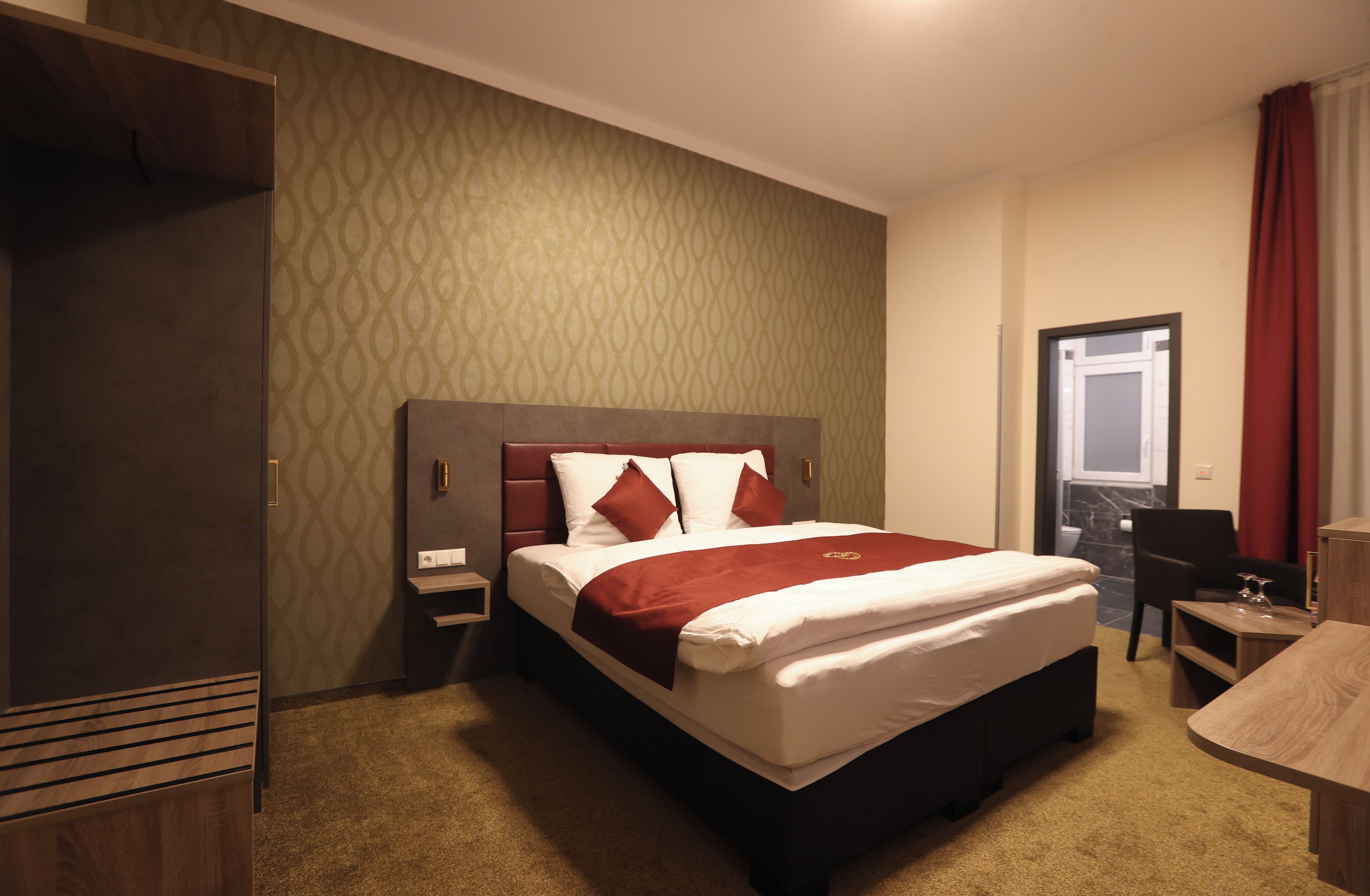 A hotel room with a large bed, a desk, a chair, and a wardrobe.