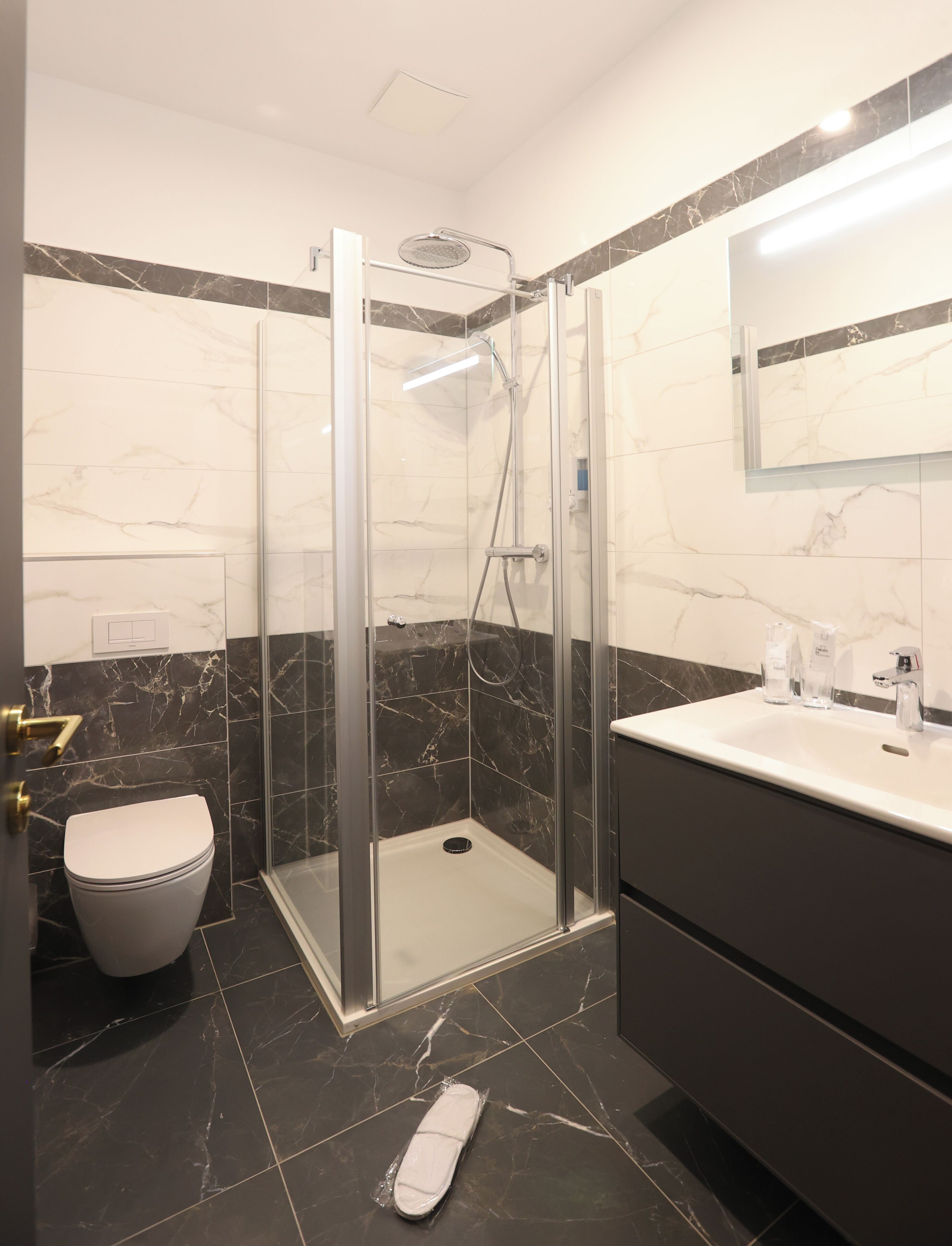 Une salle de bain moderne avec une douche à parois de verre, des toilettes blanches et un meuble-lavabo avec un miroir.