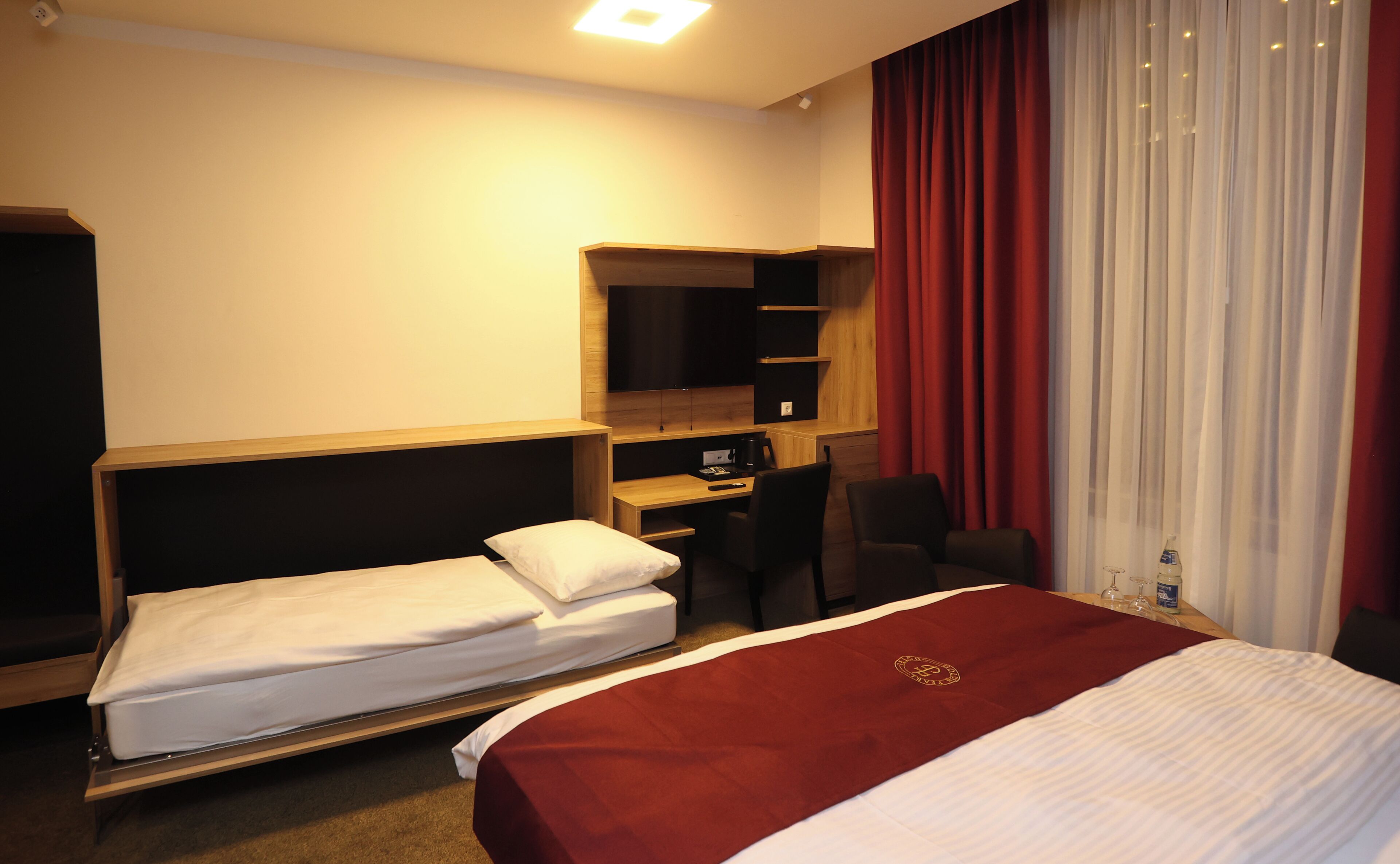 A hotel room with a bed, a desk, a chair, a wardrobe, and a TV.