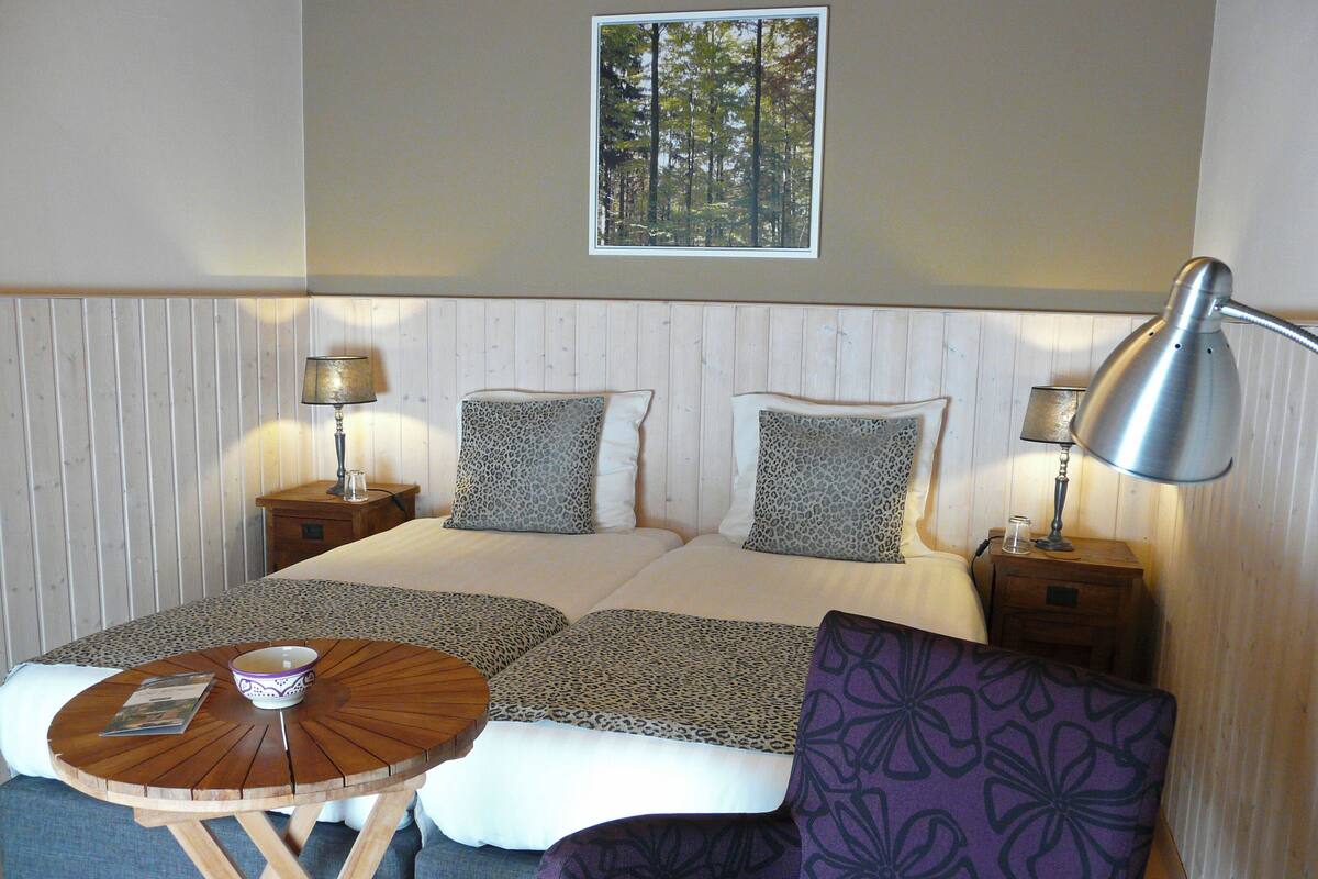 A bedroom with a bed, two nightstands, a table, a chair, and a framed picture on the wall.