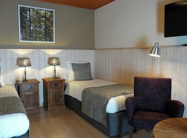 A bedroom with two beds, a nightstand, a chair, a TV, and a window with a forest view. - Landhaus Meine Auszeit (Bodenmais)