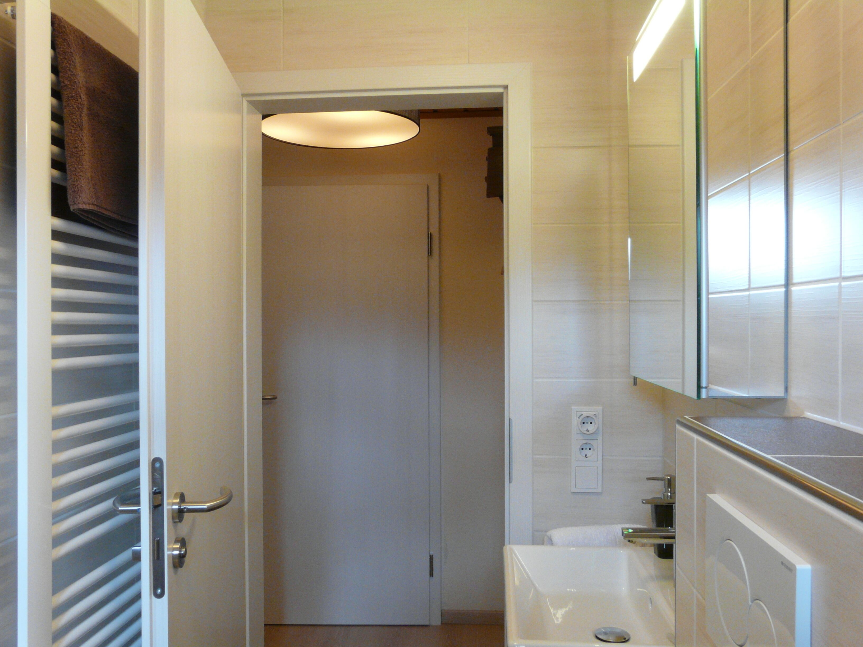 A narrow bathroom with a white door, a towel rack, a mirror, and a sink.
