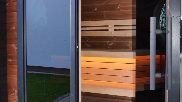 Ein modernes Gebäude mit einer Schiebetür, Holzvertäfelungen im Inneren und einem sichtbaren Außenbereich mit Rasen.