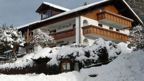 Ein mehrstöckiges Chalet mit Holzbalkonen und einer Skipiste im Hintergrund.