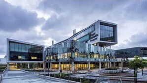 A modern building with a glass facade, a prominent entrance, and a landscaped area with pathways and seating.