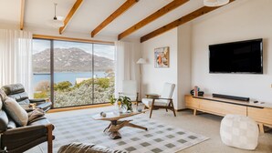A modern living room with a large window, a flat-screen TV, and a wooden ceiling. - Perfectly positioned! (Glamorgan-Spring Bay)
