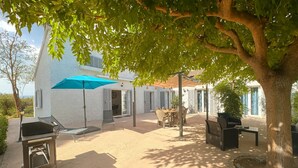 Ein Außenbereich mit Terrasse, Grill, Tisch und Stühlen sowie einem blauen Sonnenschirm.