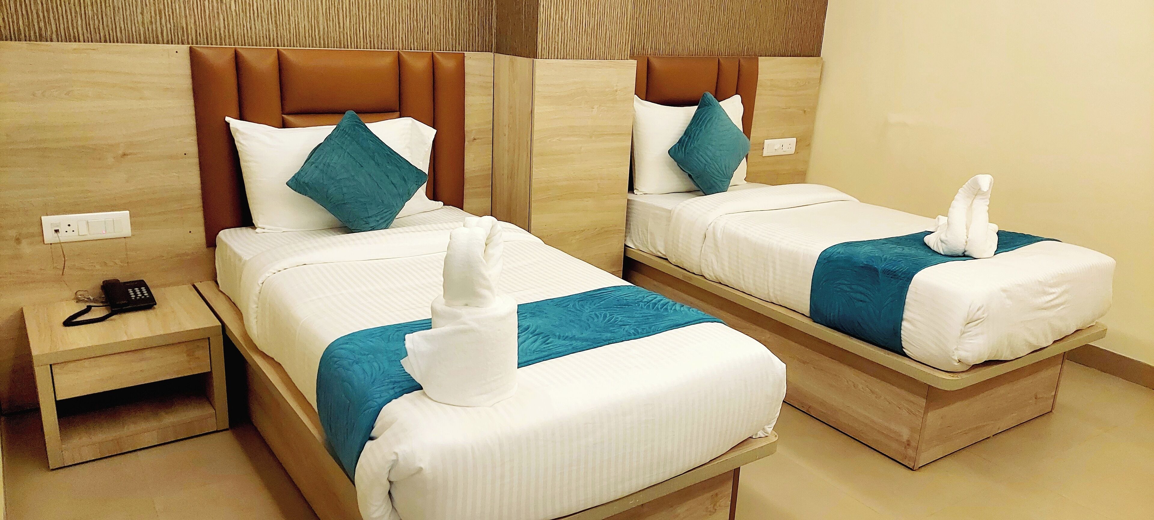 Deux lits jumeaux dans une chambre d’hôtel, avec des têtes de lit en bois, une literie blanche et des coussins décoratifs de couleur turquoise.