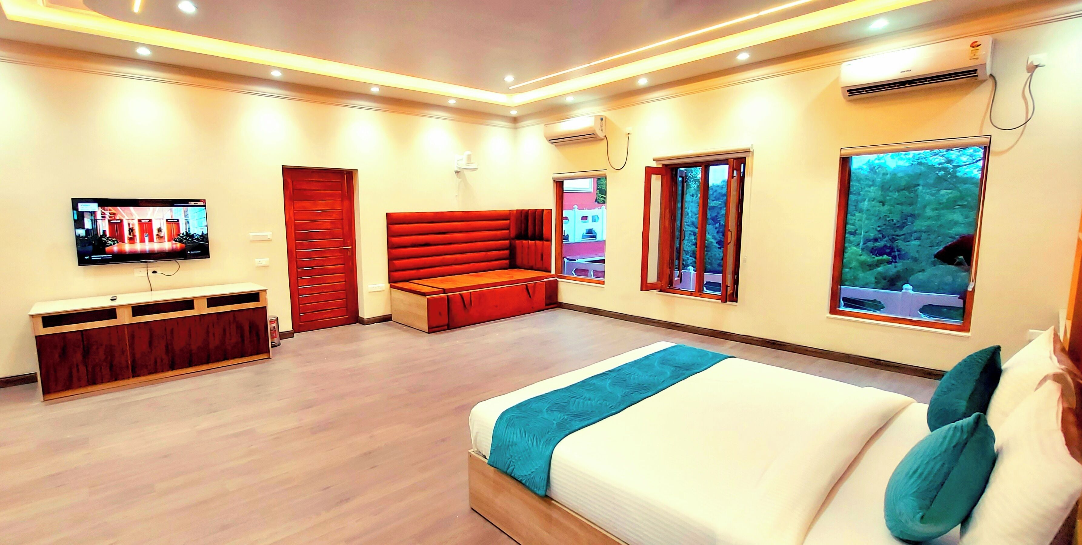 A modern hotel room with a large bed, a seating area, a TV, and a window with a view of trees.