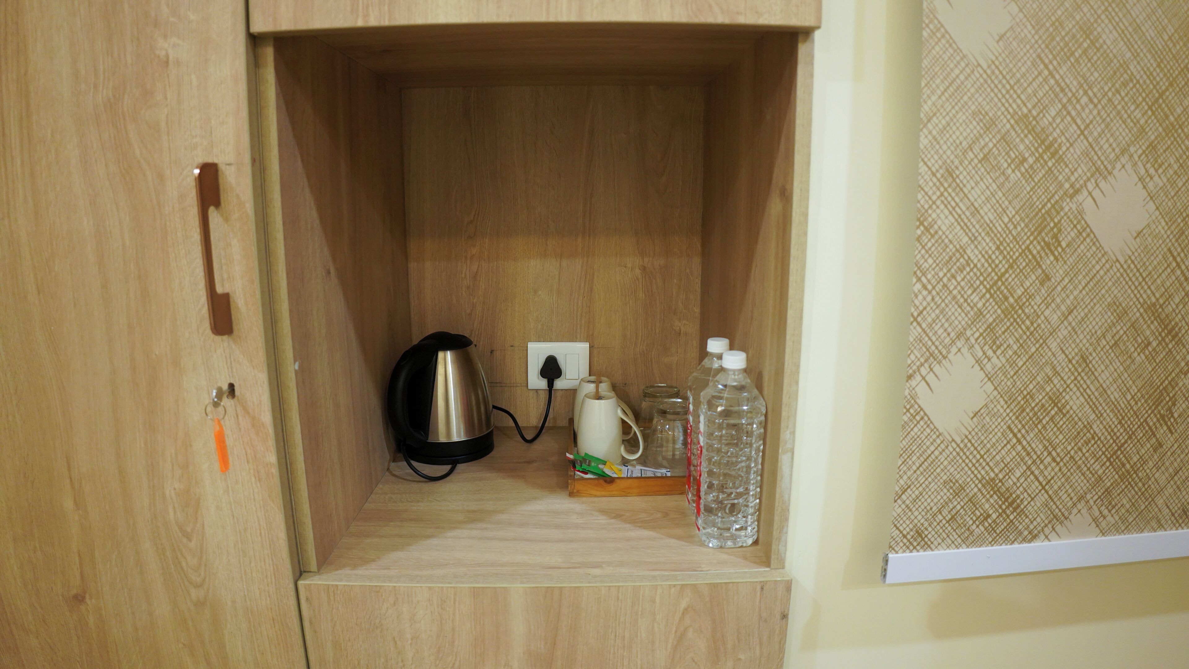 A wooden cabinet with a kettle, a coffee maker, and water bottles.