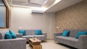 A modern living room with two grey sofas, each with a teal pillow, a wooden coffee table, and a ceiling fan. - Hotel Ananda Kashi (Varanasi)