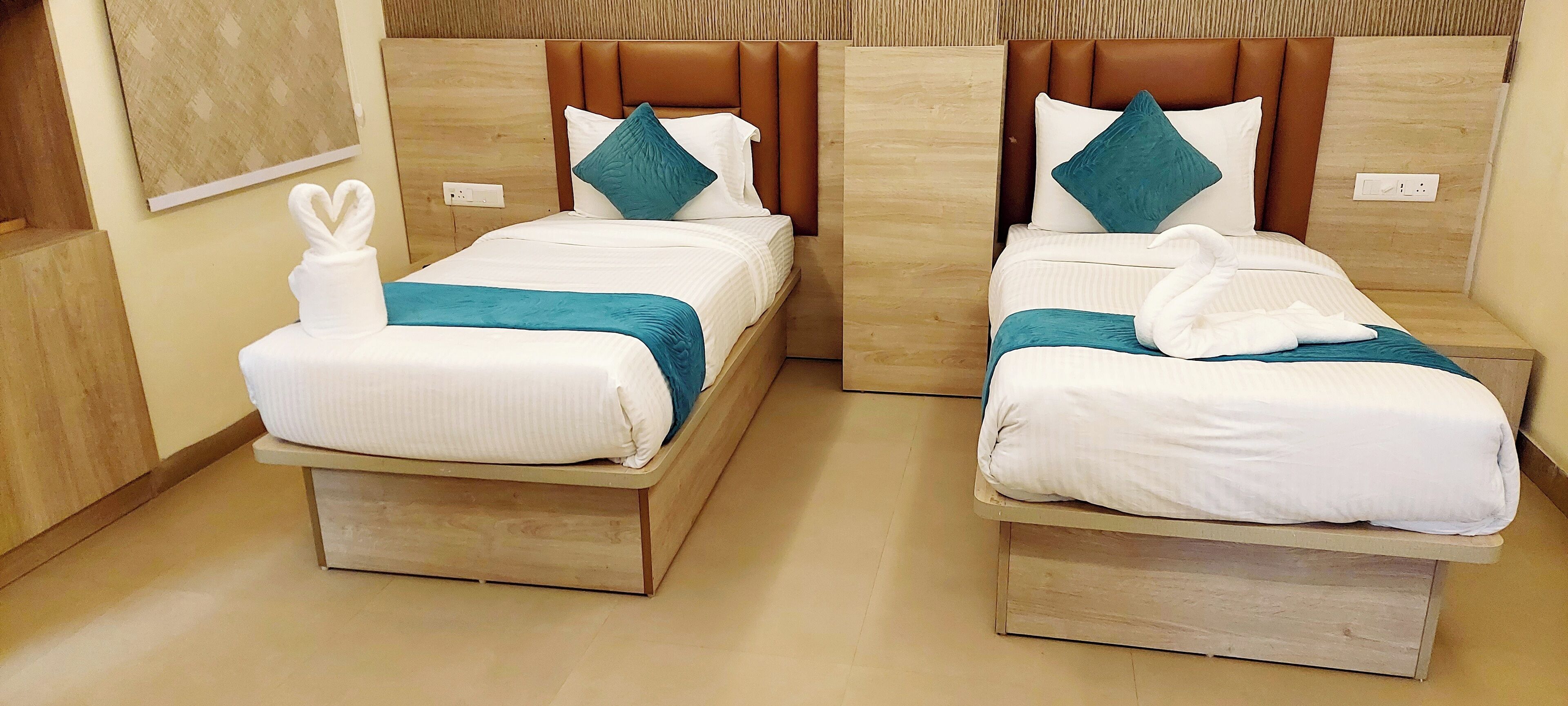 Two twin beds with wooden headboards, white bedding, teal throw pillows, and a heart-shaped towel on one bed.