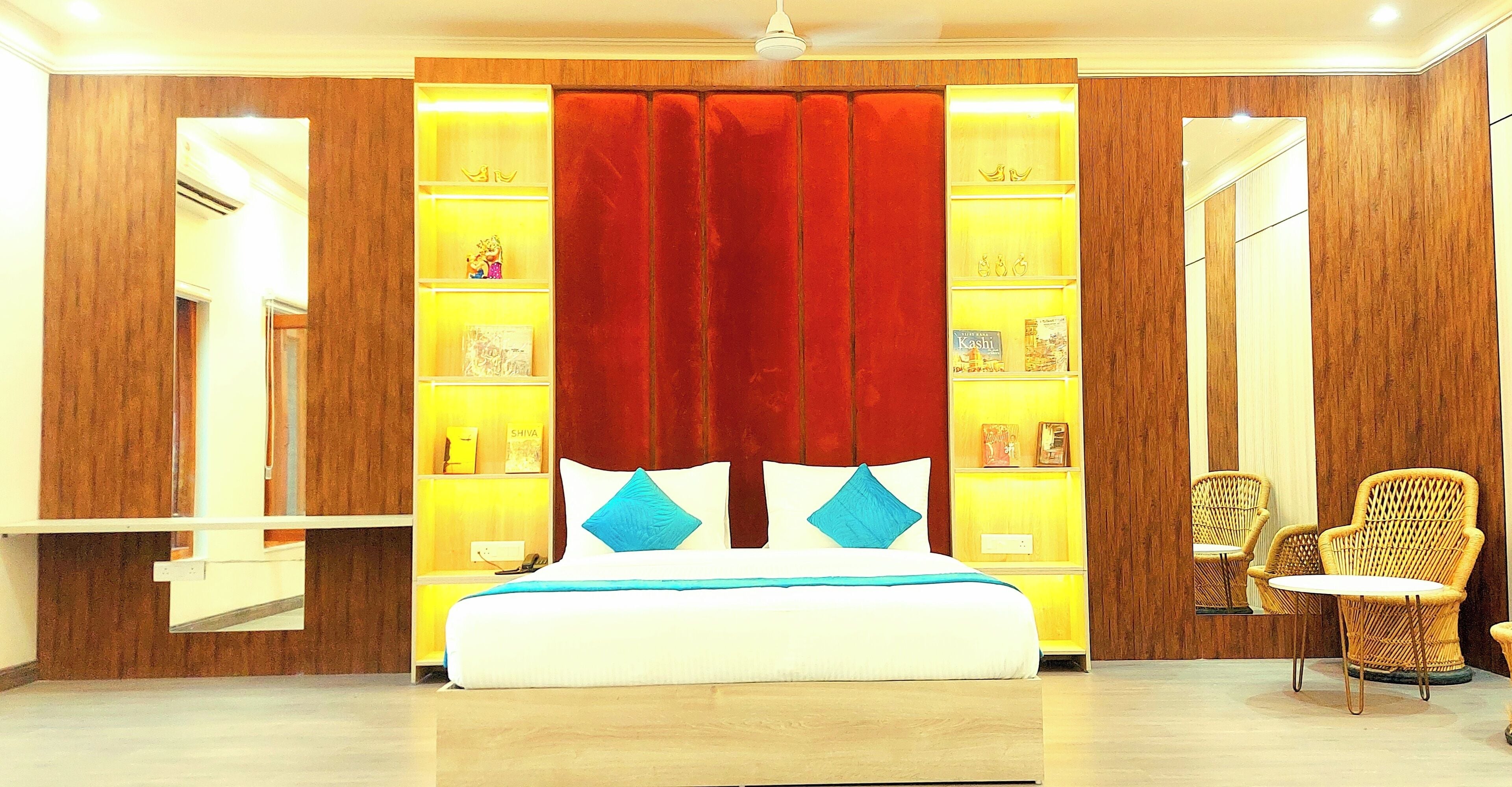 A hotel room with a bed, a red accent wall, a bookshelf, and wicker chairs.