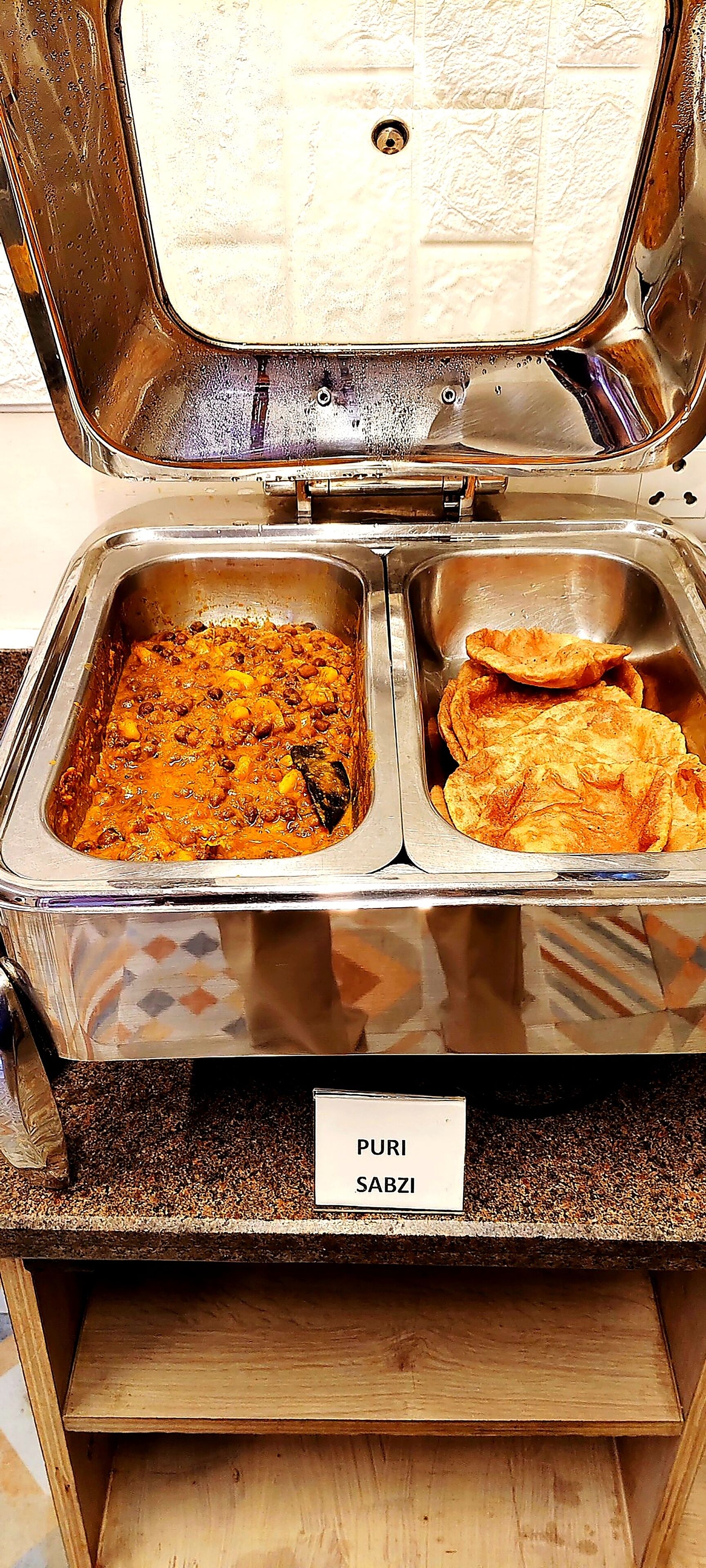 A buffet with two stainless steel serving dishes, one containing a curry and the other containing flatbreads.