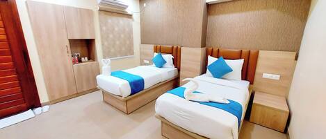 A hotel room with two beds, each with a blue bedspread and white pillows, a wooden headboard, and a small shelf with toiletries.