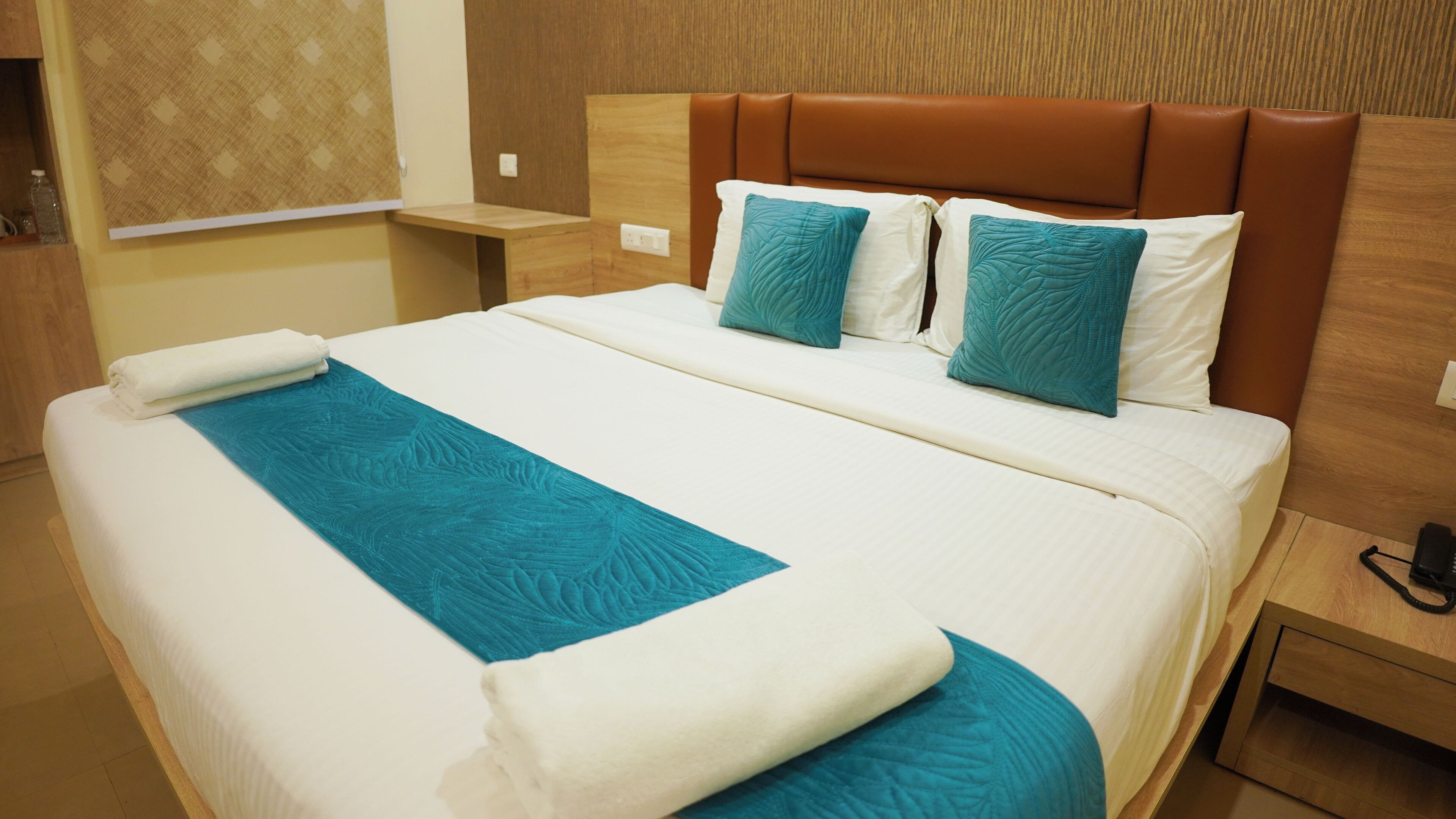 A neatly made bed with a blue accent runner, two pillows, and a brown headboard.
