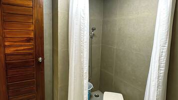 Un espacio de ducha pequeño y cerrado con una puerta de madera, una cortina de ducha blanca y un taburete pequeño.