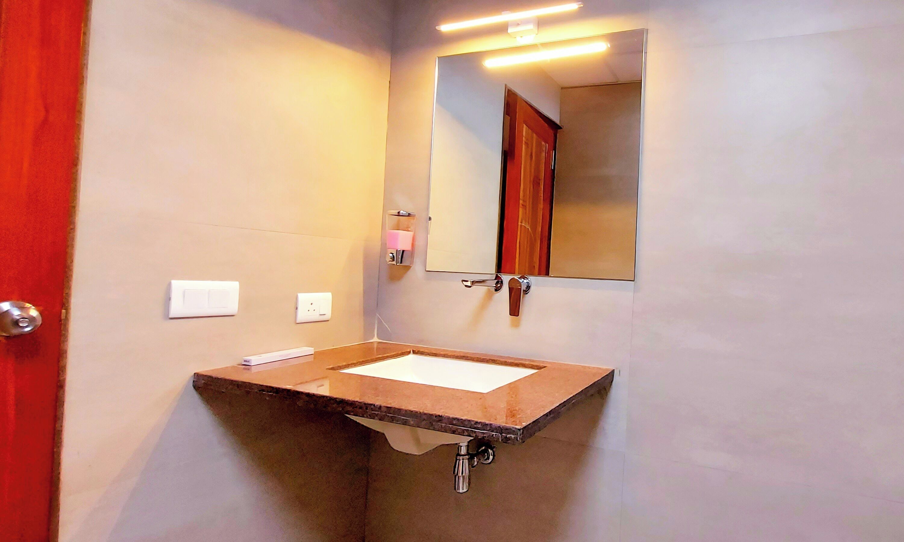 A bathroom with a sink, mirror, and a red door.