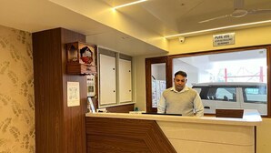 A reception desk with a 'Pure Veg' sign, a wooden panel design, and a view of a vehicle outside. - Hotel Ananda Kashi (Varanasi)