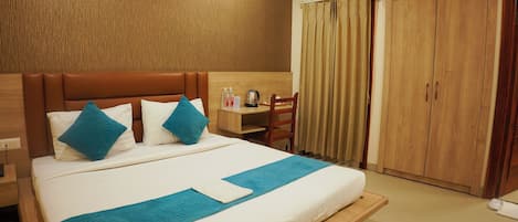 A hotel room with a large bed, a wooden headboard, a desk with a chair, and a wardrobe.