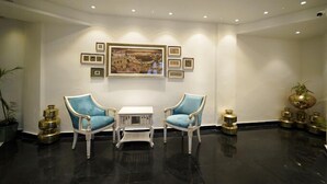 A lobby with two blue chairs, a small table, and a large framed painting on the wall. - Grandrosse Boutique - Lake Facing Hotel (Udaipur)