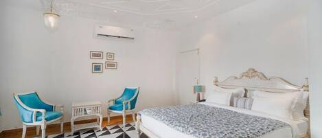 A bedroom with a bed, two chairs, a small table, and a ceiling fan.