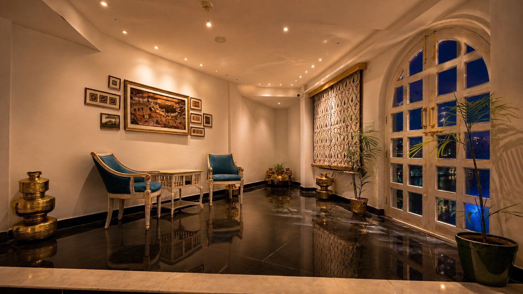 Um hall com piso lustroso, duas poltronas azuis revestidas, uma mesa branca e uma grande janela em arco com vários painéis.