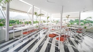 A rooftop restaurant with outdoor seating, white tables and chairs, and potted plants. - Grandrosse Boutique - Lake Facing Hotel (Udaipur)