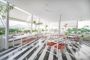 Un restaurante en la azotea con mesas y sillas blancas al aire libre, y plantas en macetas.