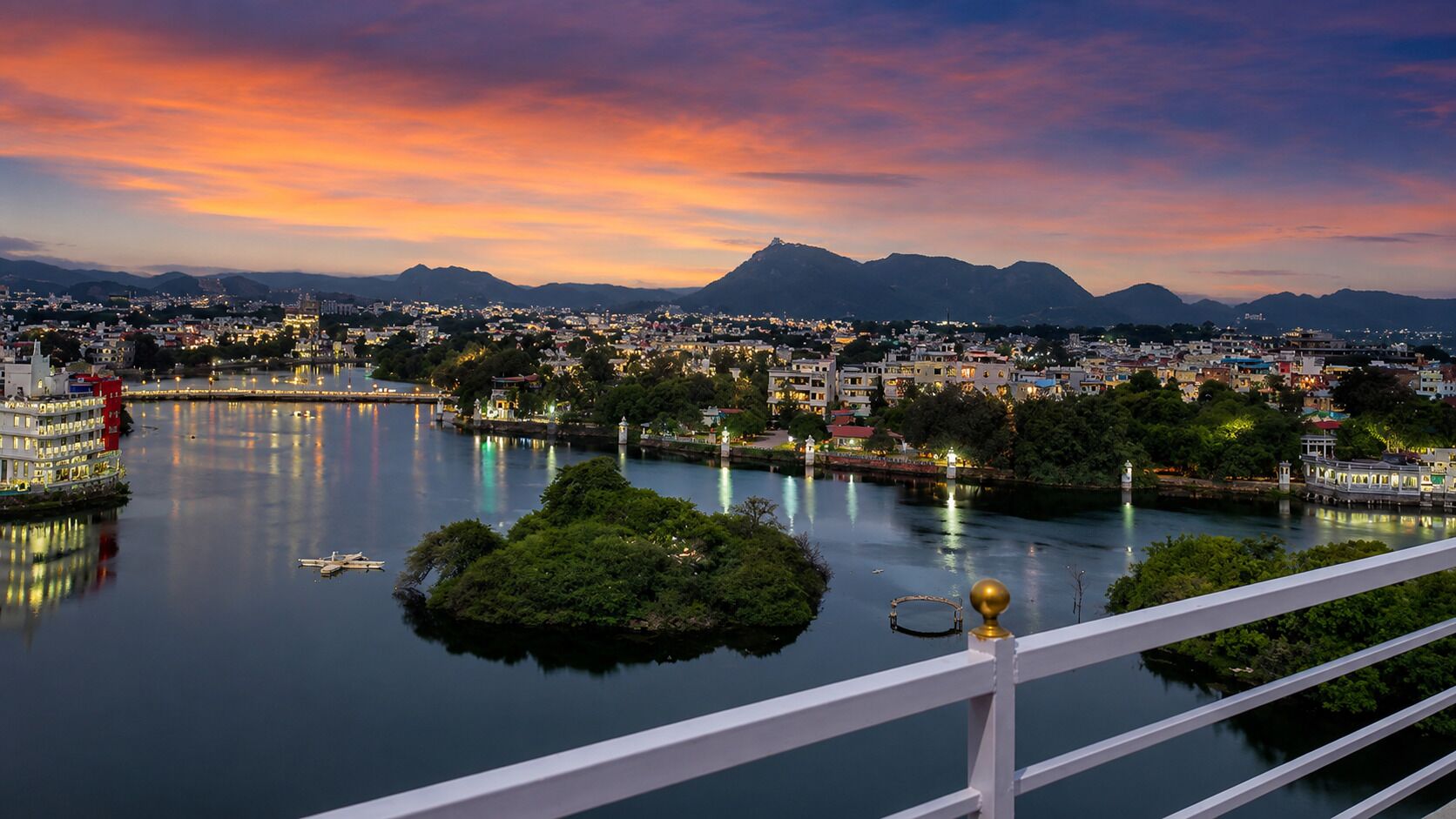 A cityscape at dusk with a river, buildings, and a mountain in the background.
