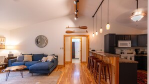 Een moderne woonkamer met een blauwe modulaire bank, houten vloeren en een keuken met donkere kasten en een witte magnetron.