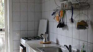 Une cuisine avec des meubles blancs, un évier en acier inoxydable et une cuisinière à gaz. Des ustensiles de cuisine sont suspendus au mur, et un égouttoir à vaisselle y est également fixé.