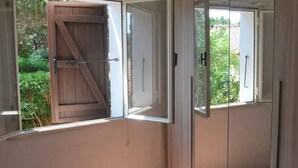 Une chambre avec un lit, une porte-fenêtre coulissante et une fenêtre avec un volet en bois.