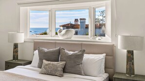 A bedroom with a large window, a bed with multiple pillows, and two bedside lamps.