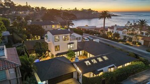 A coastal residential area with modern houses, a street, and a view of the ocean at sunset.