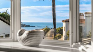 A view from a window overlooking a coastal area with palm trees and a clear sky.